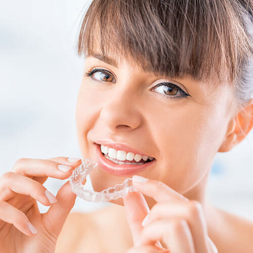 Woman holding an Invisalign® aligner as part of our dental services in Woburn, MA