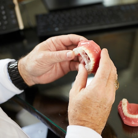 A dentist fitting a patient's Invisalign® aligner over artificial teeth