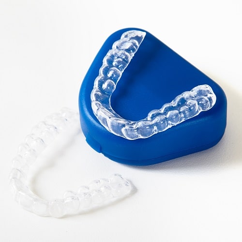 A clear, polymer appliance device sitting in it's blue tray. A dental appliance is sometimes used for TMJ treatment in Woburn, MA