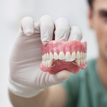 Doctor wearing white medical glove holding a set of partial dentures.